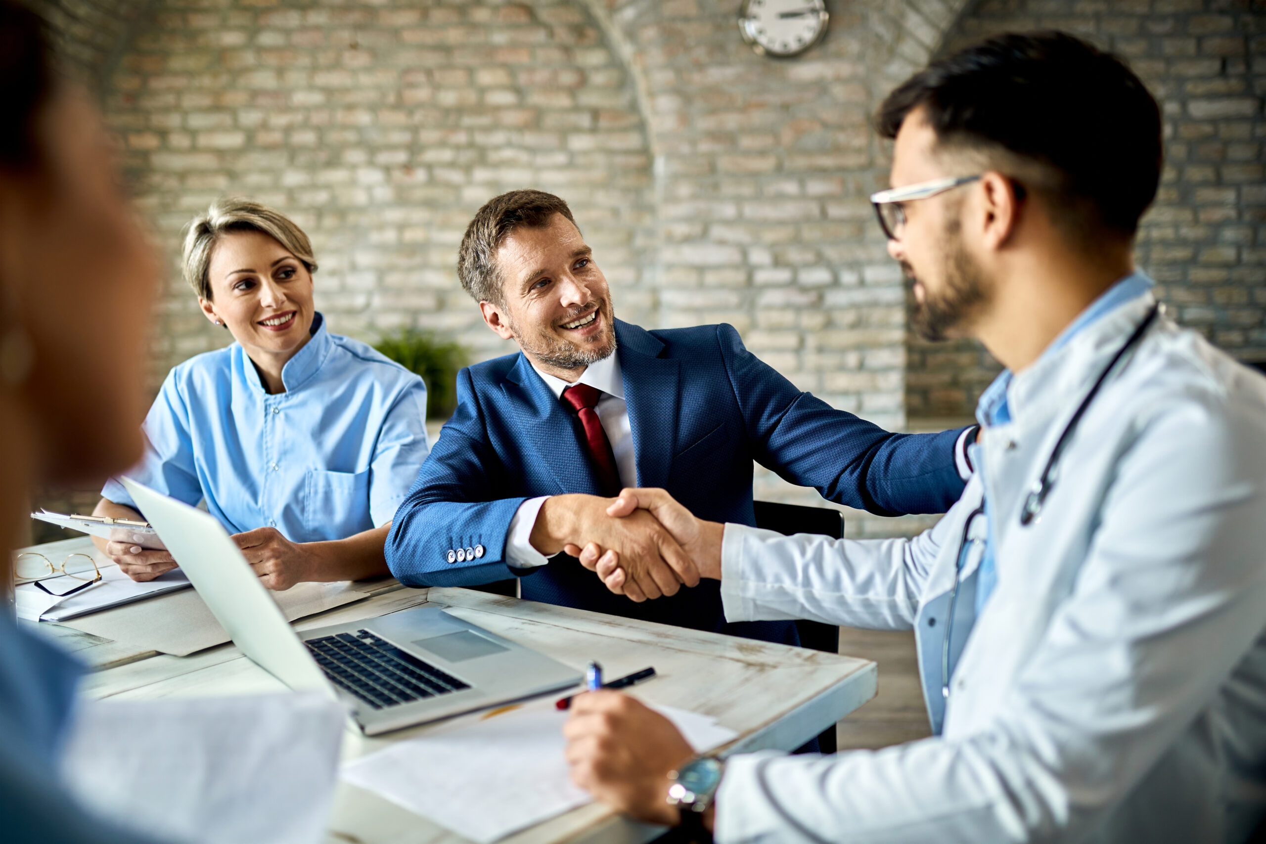 Happy financial advisor and male doctor shaking hands after successful meeting in the office.